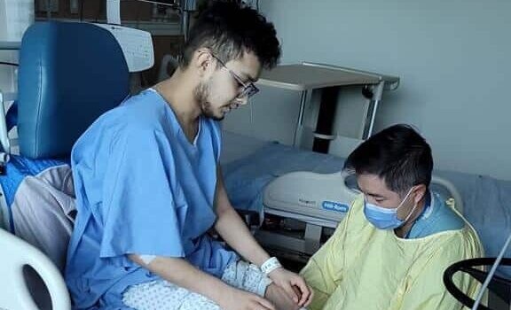 El joven Josue Flota en el hospital después de su cirugía siendo ayudado por un enfermero.
