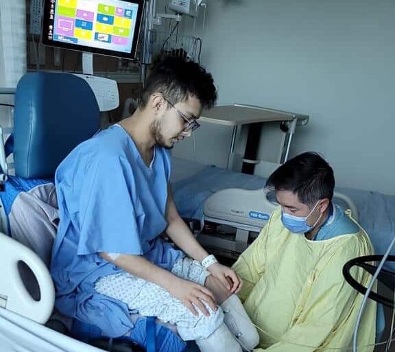 El joven Josue Flota en el hospital después de su cirugía siendo ayudado por un enfermero.
