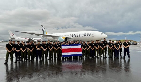 Un grupo de bomberos costarricenses frente a un avión y junto a la bandera de Costa Rica.