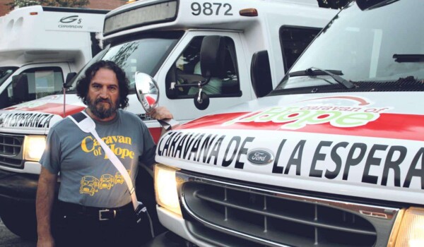 Hombre parado enfrente de varias ambulancias marcadas con el nombre 